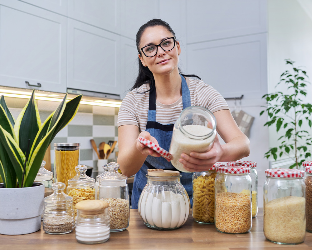 Жена в кухнята показва буркани за съхранение на суха храна