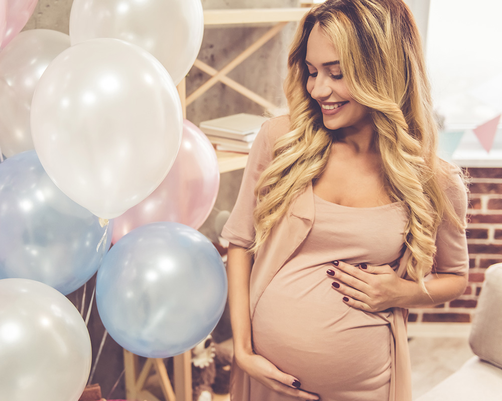 Бременна жена с усмивка поглежда към цветните балони на baby shower