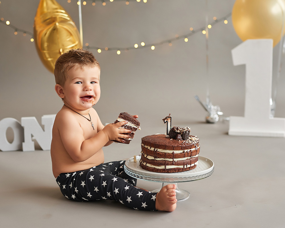 Едногодишно момченце държи в ръцете си парче шоколадова торта за рождения си ден