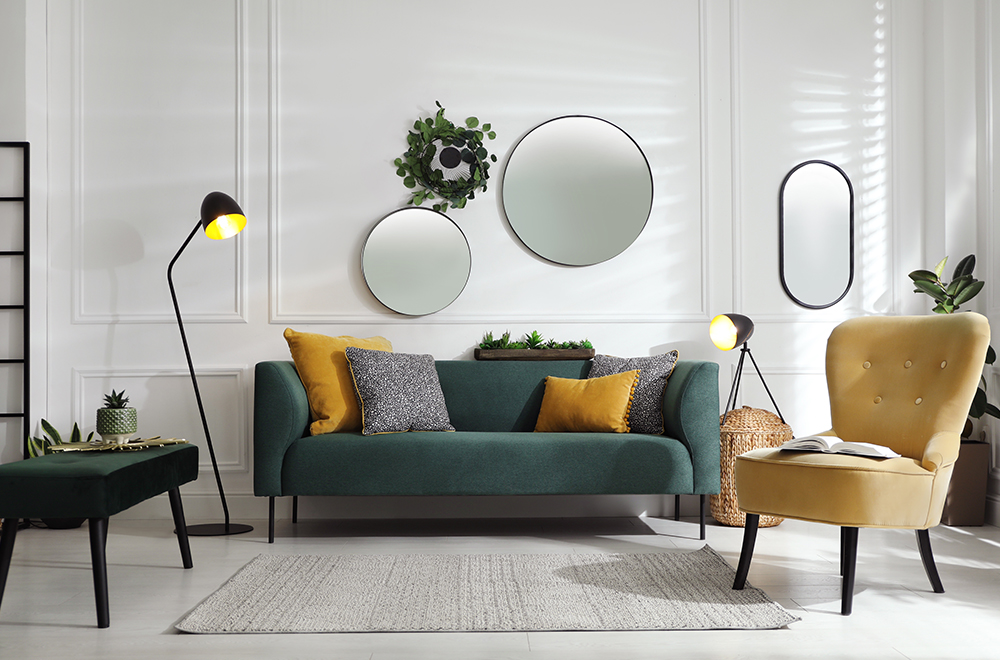 Модерен хол в светли цветове със зелено канапе, жълти възглавници и кръгли огледала на стената.