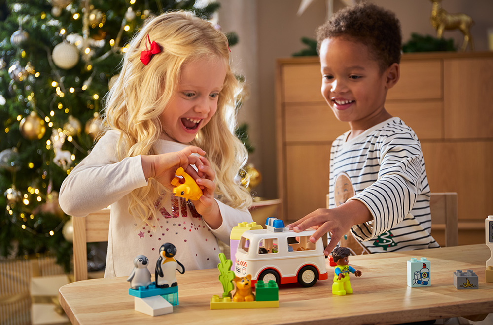 Две деца играят с LEGO блокчета под елхата.