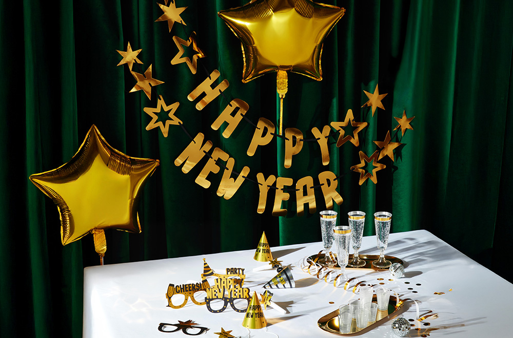 Маса, декорирана за Нова година, с балони, чаши и златни украшения.