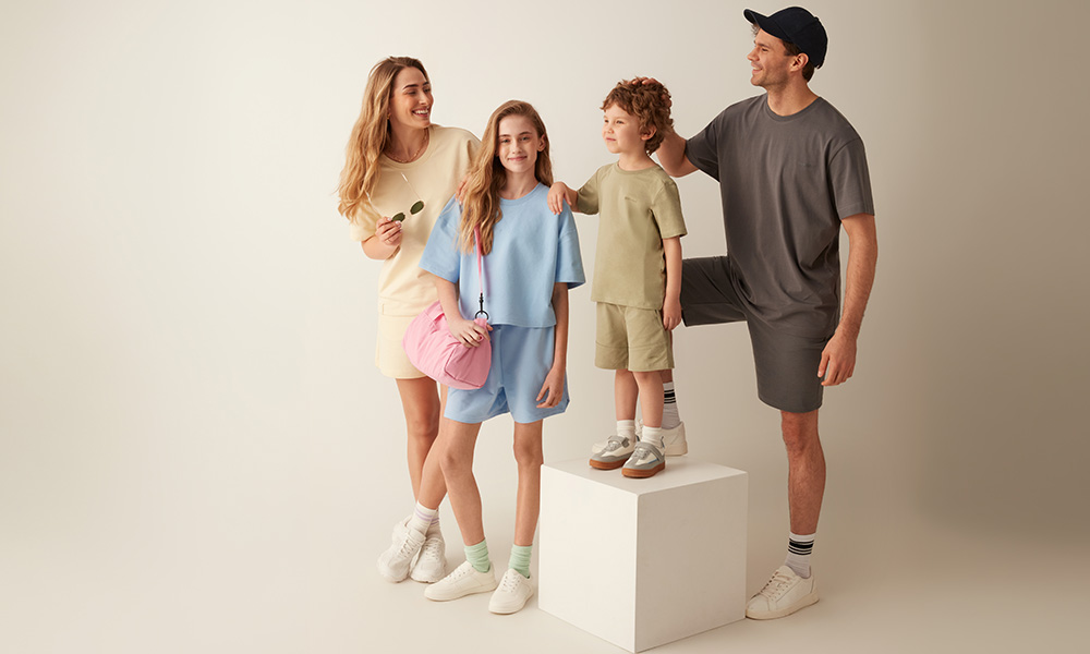 Семейство в пастелни дрехи позира заедно на светъл фон.